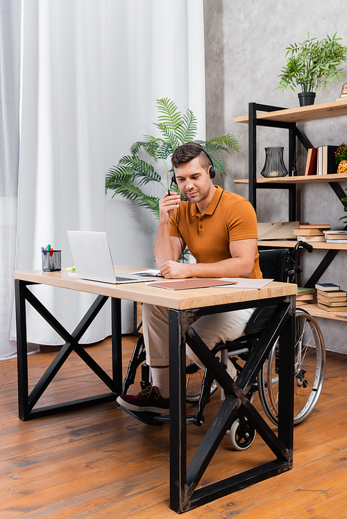 young handicapped man in headset working in home office near laptop