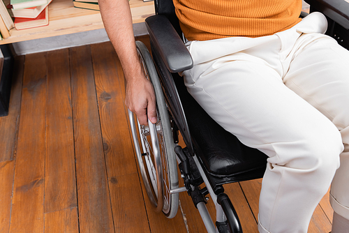 cropped view of disabled man sitting in wheelchair at home