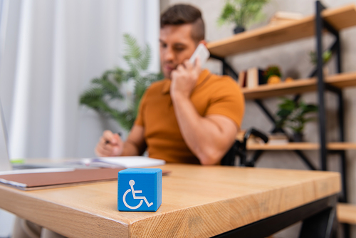 selective focus of cube with disability sign near man talking on smartphone on blurred background