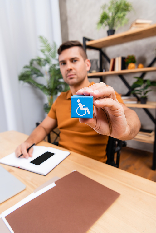 selective focus of cube with disability sign in hand of freelancer working at home