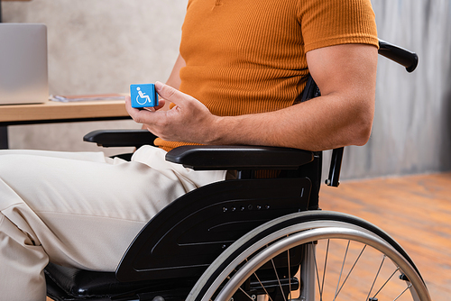 cropped view of man in wheelchair holding cube with disability sign