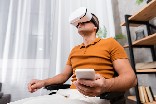 low angle view of handicapped man holding smartphone while gaming in vr headset