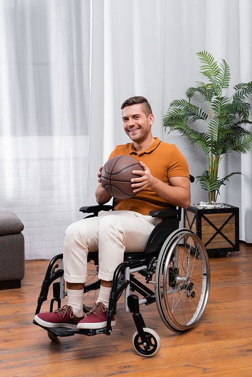 joyful handicapped man holding basketball while sitting in wheelchair