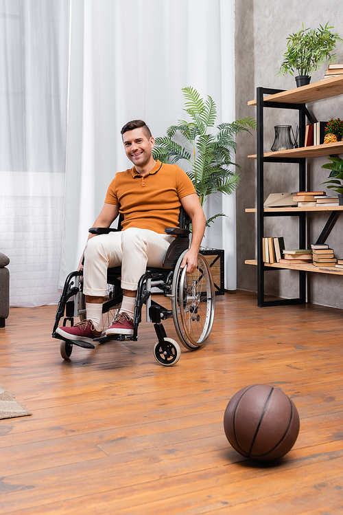 positive disabled man sitting in wheelchair near basketball on floor