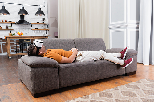 young man in casual clothes relaxing in vr headset on sofa at home