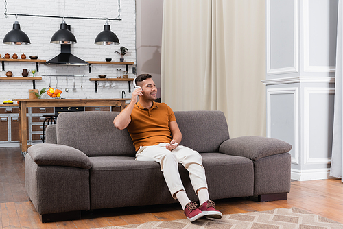 smiling man adjusting headphones while listening music on couch at home