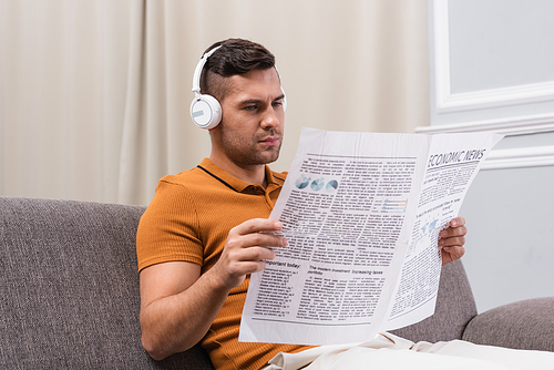 young man reading newspaper while listening music in wireless headphones