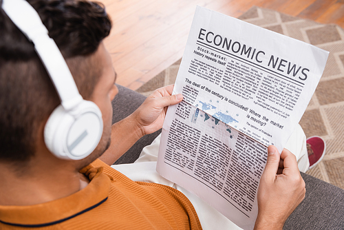 overhead view of man in headphones reading economic news on blurred foreground