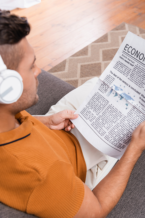 overhead view of blurred man in headphones reading newspaper at home
