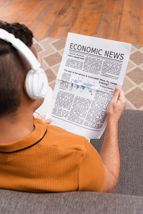 overhead view of man in wireless headphones reading economic news on blurred foreground