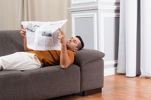 man lying on sofa and reading newspaper at home