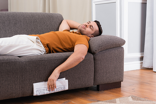 young man sleeping on couch while holding newspaper
