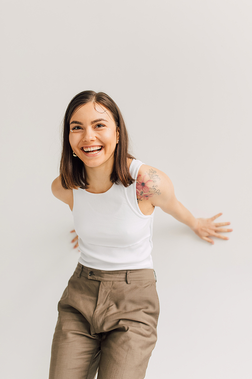 laughing young woman in white top and beige trousers on gray background