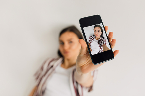 smartphone with selfie picture of young woman with duck face grimace on blurred background