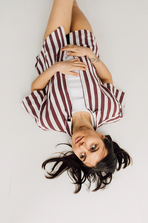 top view of dreamy young woman in striped shirt lying on grey background
