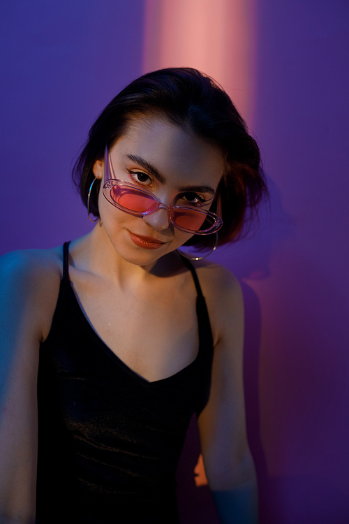 young adult woman in black tank top and sunglasses  on violet and pink background