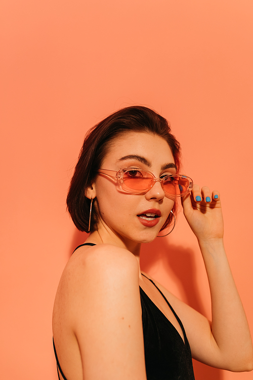 young woman in sunglasses with half-opened mouth on orange background