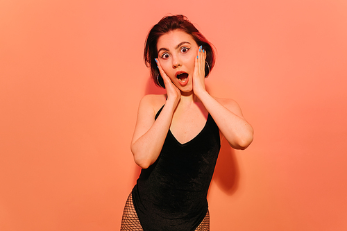 excited young woman grimacing with hands near face on orange background