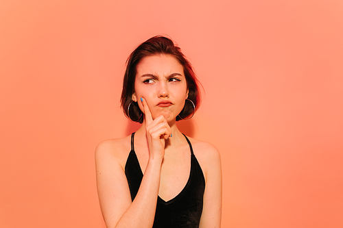 thoughtful young woman looking away holding hand near face on orange background