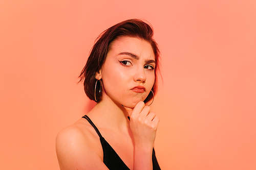 thoughtful young woman looking away with hand near face on orange background
