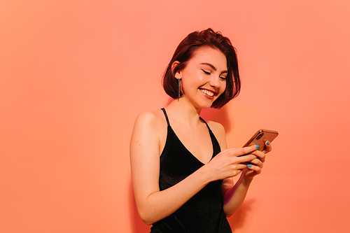 happy young woman with cellphone in hands on orange background
