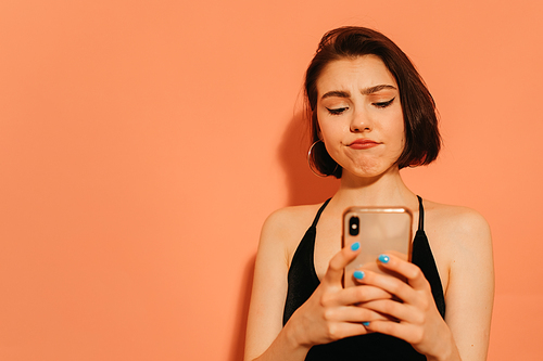 young woman looking at smartphone in hands on orange background