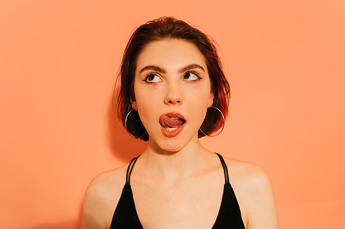 dreamy young woman grimacing with sticking out tongue on orange background