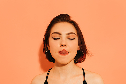 young woman grimacing with sticking out tongue on orange background
