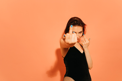 young woman with provocative middle fingers gesture on orange background