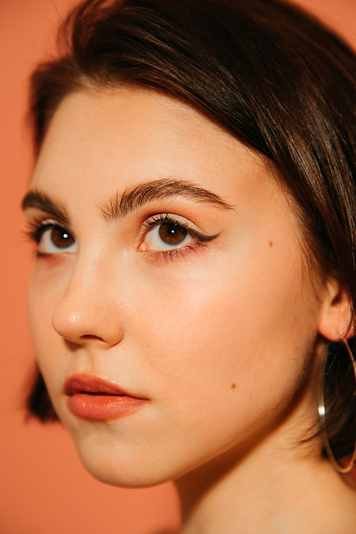 close up of young woman face with shiny summer cat eyes makeup isolated on orange