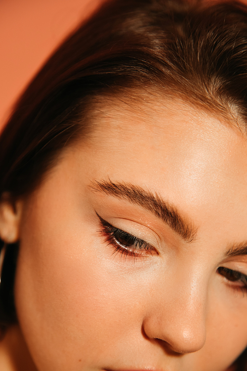 close up of young woman cropped face with shiny summer cat eyes makeup isolated on orange