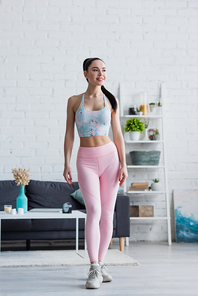 smiling woman in sports bra and leggings looking away at home