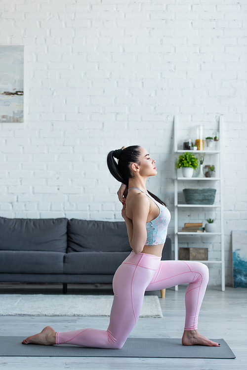 side view of brunette woman practicing crescent lunge on knee pose at home