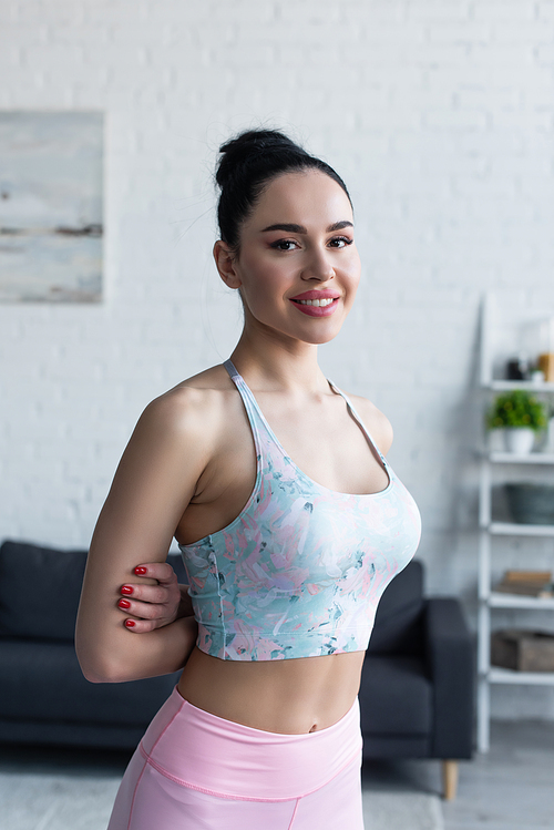 pretty woman in sports bra smiling at camera while standing with hands behind back