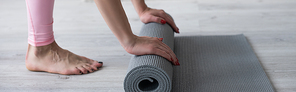 cropped view of barefoot woman unrolling yoga mat on floor, banner