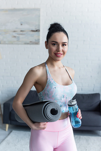 happy woman with sports bottle and fitness mat smiling at camera