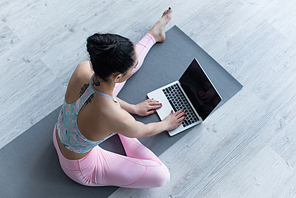 overhead view of woman in sportswear using laptop while sitting on yoga mat