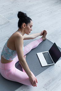 sportive woman stretching in yoga pose near laptop with blank screen