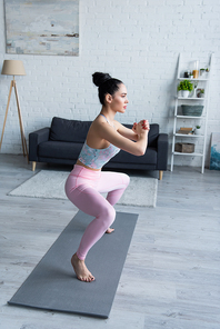 pretty woman standing in chair pose with clenched hands while practicing yoga at home