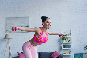 young sportive woman exercising with dumbbells and smiling at home