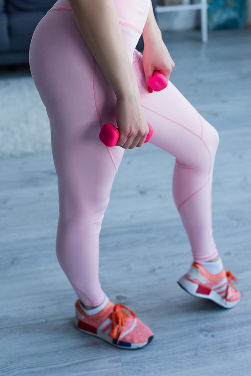 cropped view of sportswoman in leggings holding dumbbells