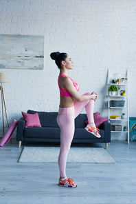 side view of young sportswoman exercising in knee to chest pose at home
