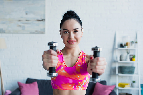 cheerful woman smiling at camera while exercising with dumbbells