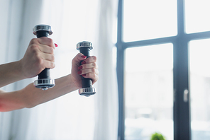 cropped view of woman exercising with dumbbells at home