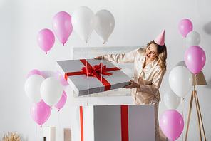 Astonished woman opening big gift box during birthday party at home