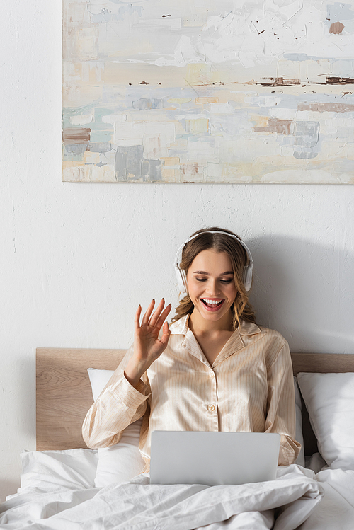 Smiling woman in headphones having video call on laptop in bedroom