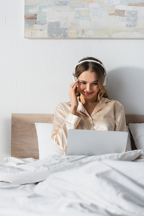 Smiling woman in headphones using laptop on bed