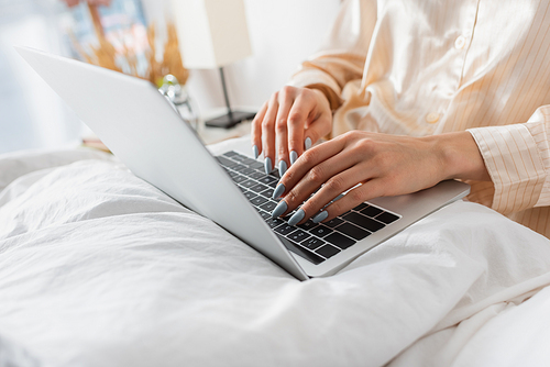 Cropped view of woman in pajama using laptop on blanket