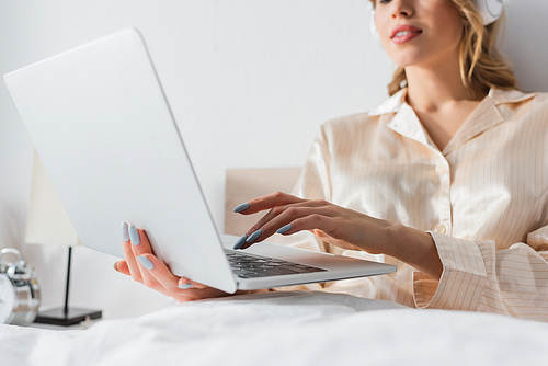 Cropped view of blurred woman in headphones using laptop on bed