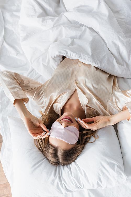 Top view of smiling woman in sleeping mask lying on bed